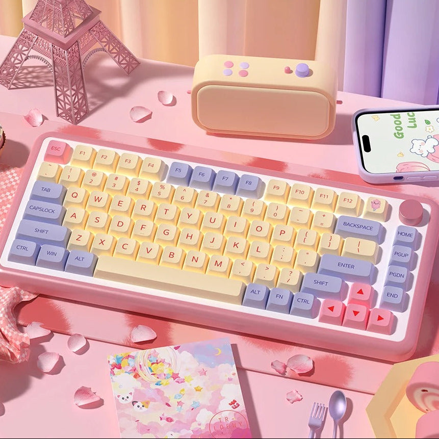 Colorful keyboard with keycaps on a pink desk setup, including a phone and Eiffel Tower model.